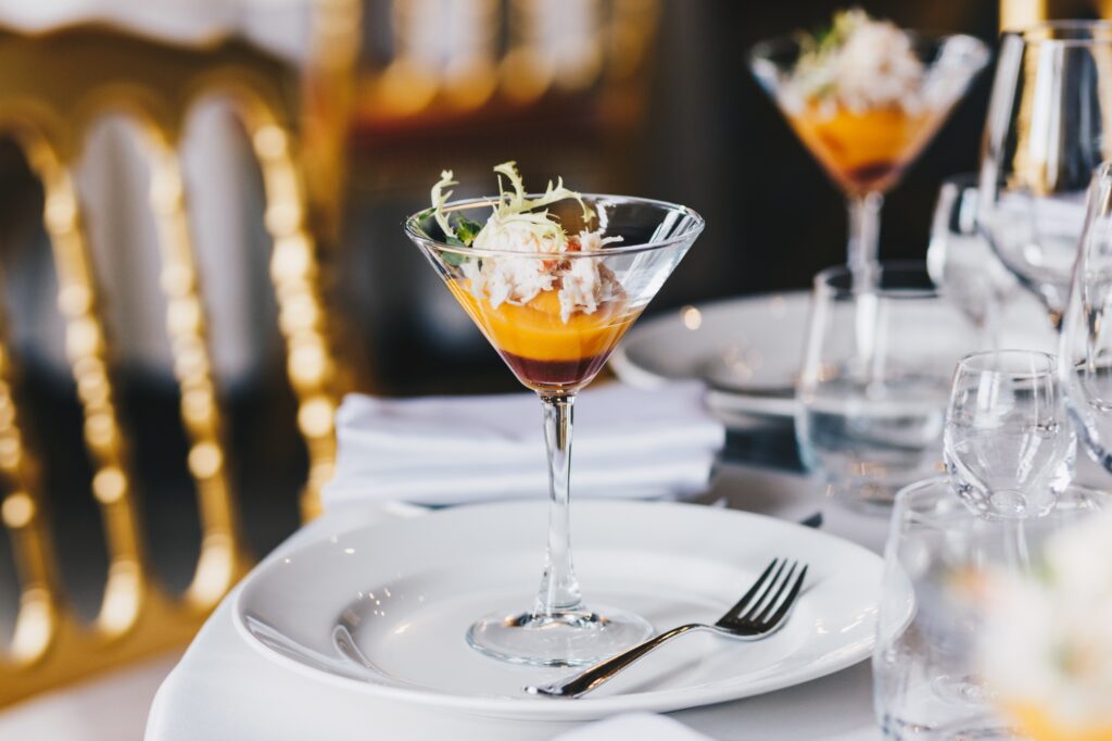 Served table with glass of cocktail, white plate with fork, with no people. Luxury restaurant